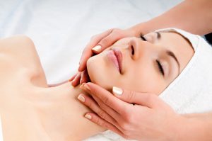 Beautiful young woman receiving facial massage with closed eyes in a spa center